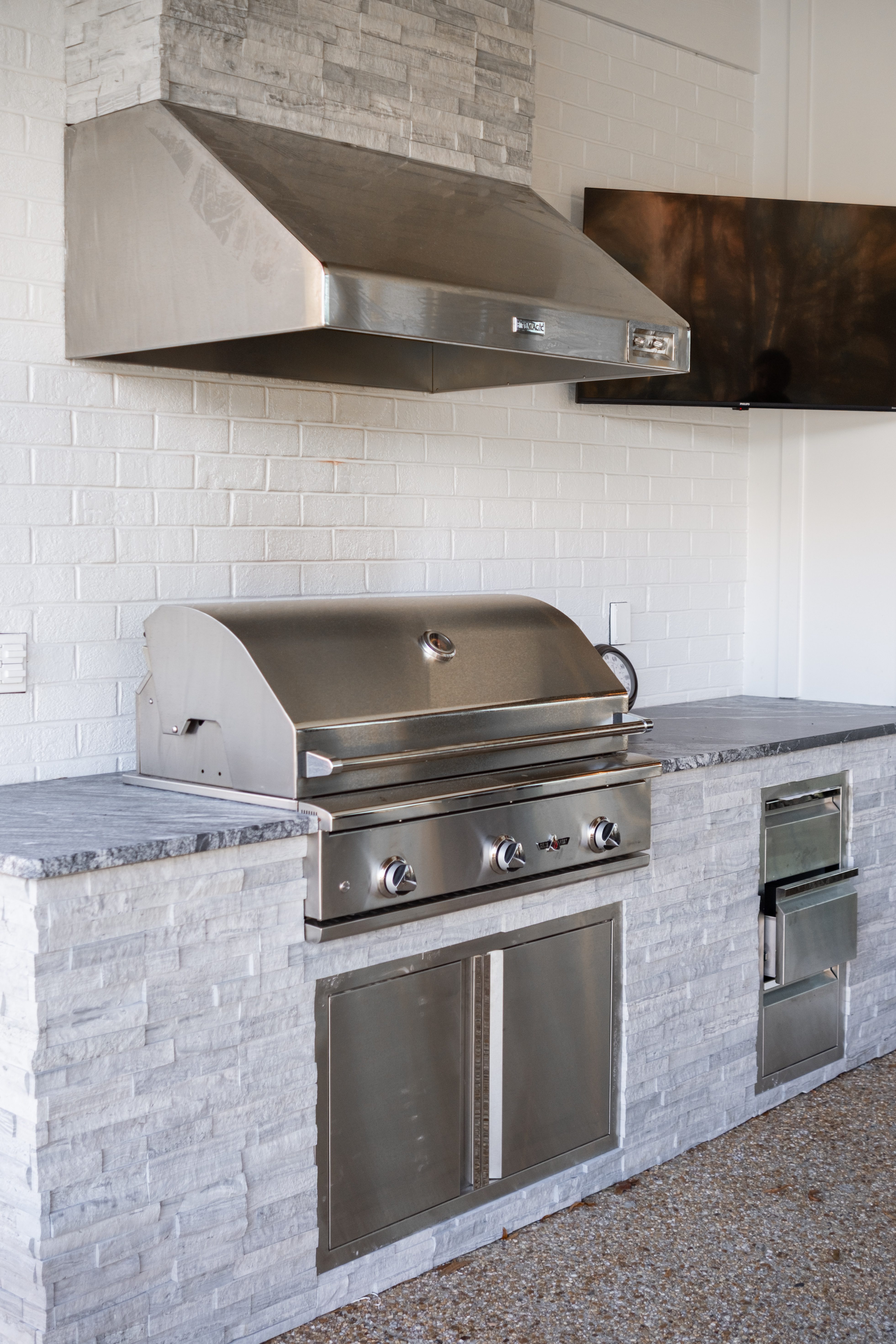 Outdoor kitchen featuring Thunder Black Leathered Granite countertops with stainless steel grill, vent hood, and stacked stone surround
